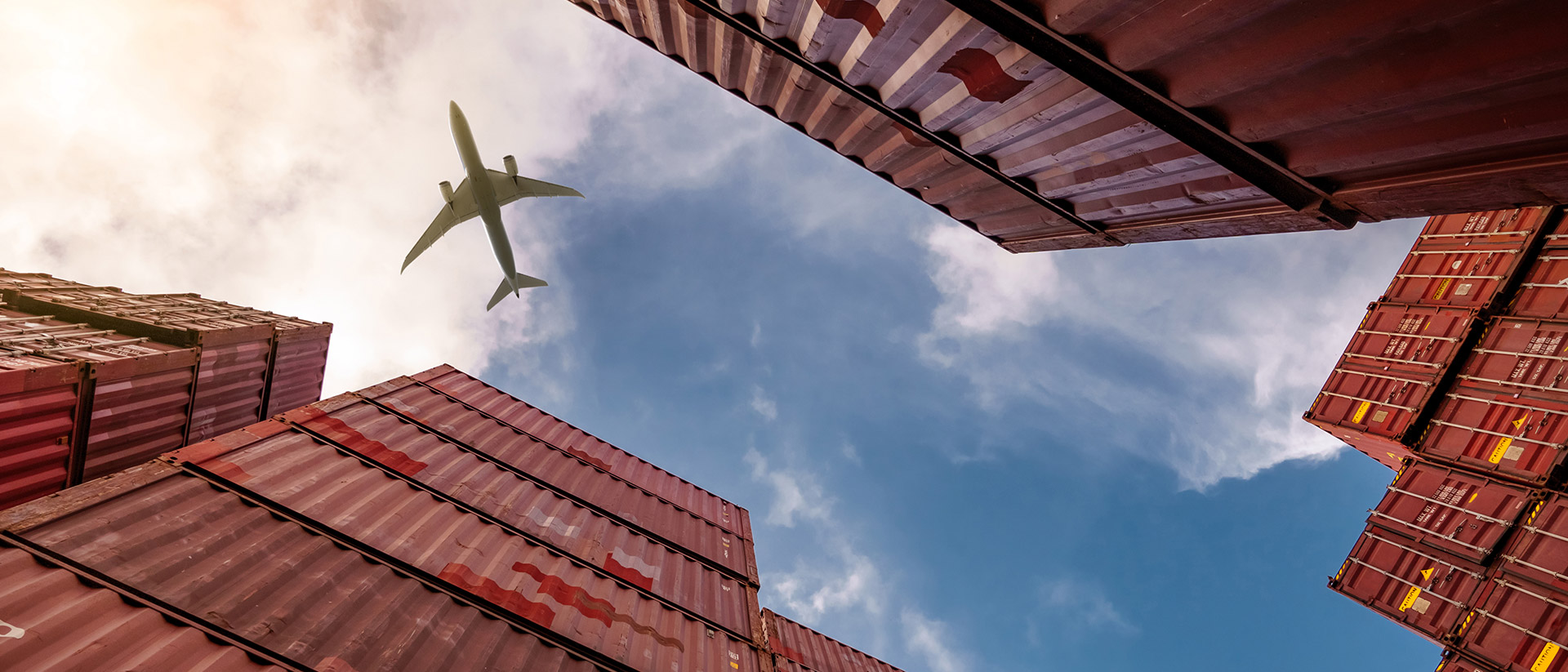 Flugzeug fliegt am Himmel, rechts und links sind Container zu sehen.